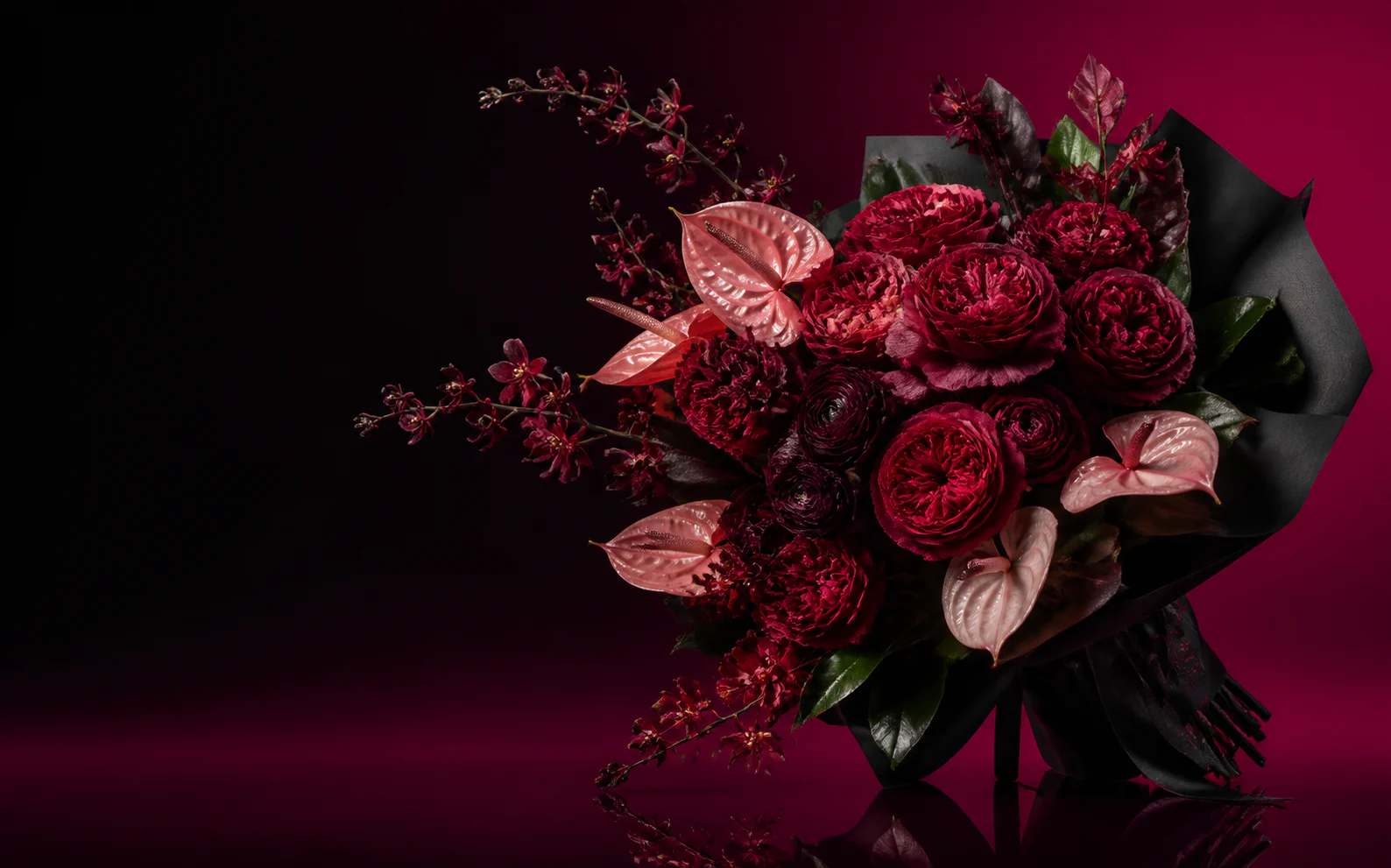 Buchet sculptural cu trandafiri bordo și anthurium roz, fotografiat pe fundal negru și zmeuriu